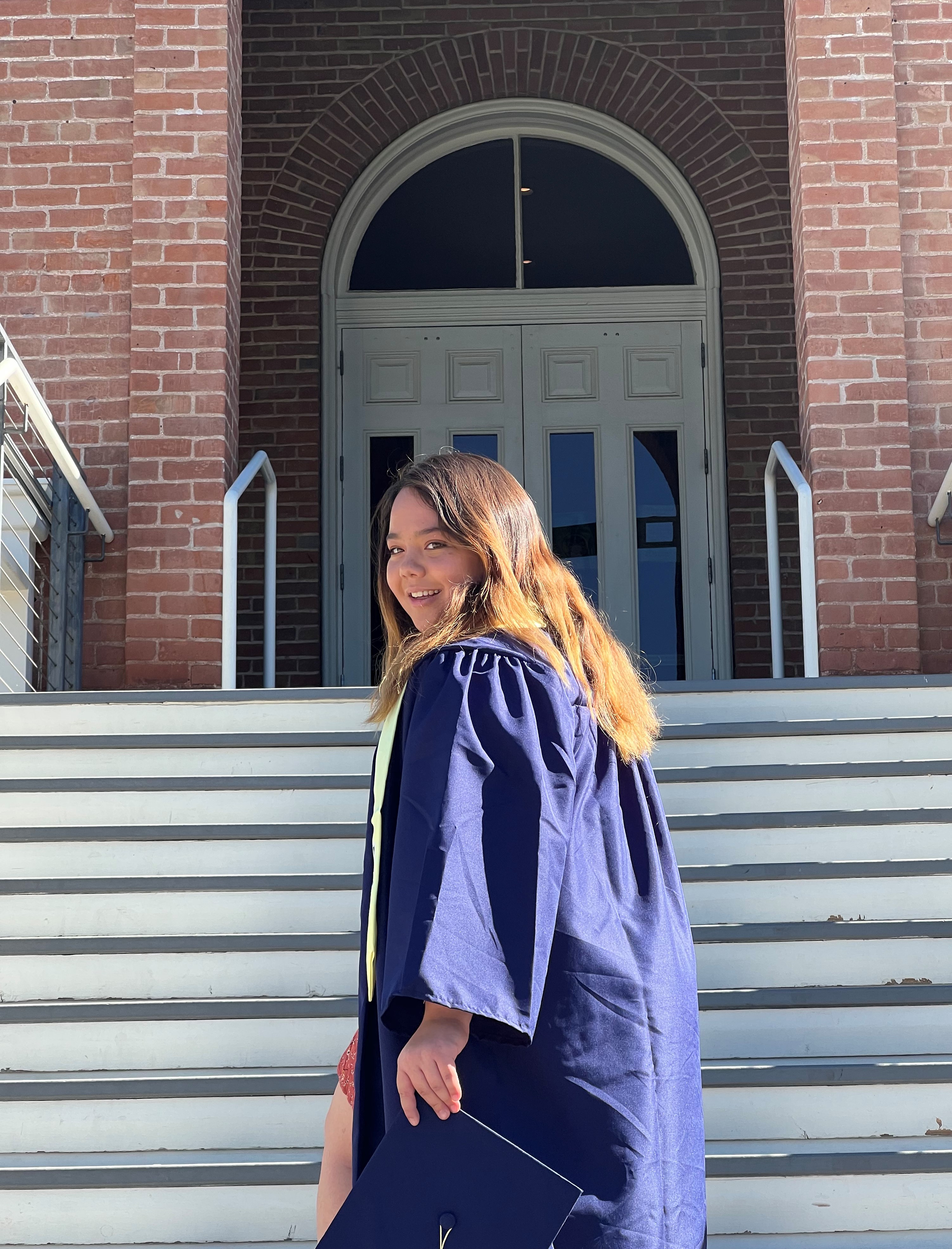 Student posing in front of Old Main in blue cap and gown regalia