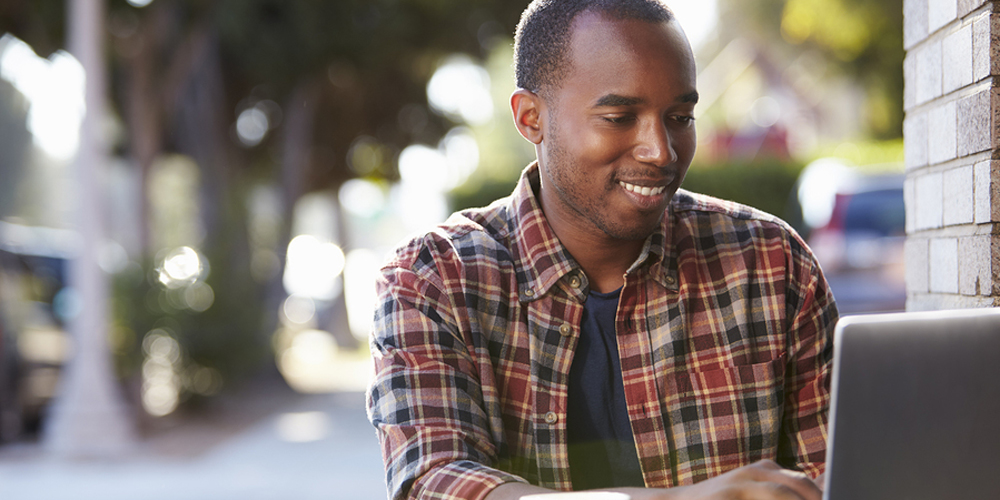 Male student smiling while looking at laptop, University of Arizona