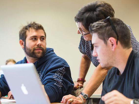 two male students and instructor looking at laptop, in classroom, University of Arizona, Tucson