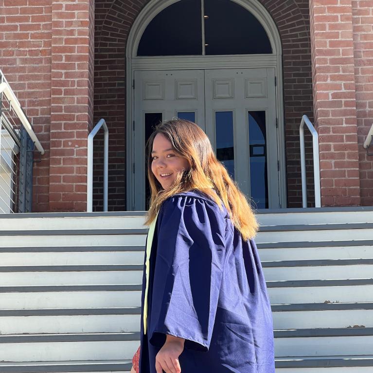 Student posing in front of Old Main in blue cap and gown regalia